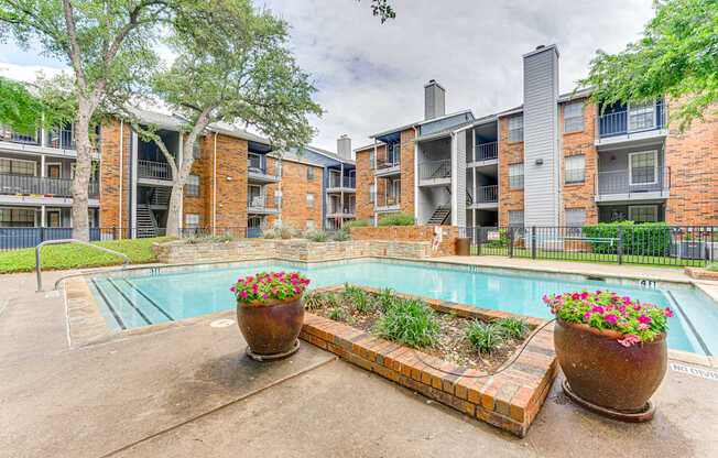 A pool surrounded by a brick border with two large flower pots in the foreground.