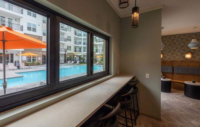 A room with a bar and a view of a pool and apartment building.