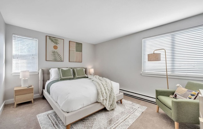 A bedroom with a large bed, a green chair, and two lamps.