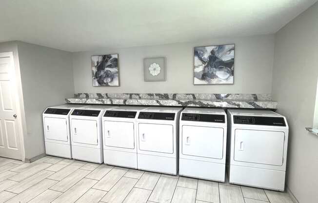 a row of white washers and dryers in a laundry room with a row