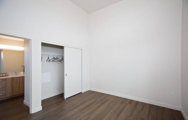 a bedroom with white walls and wood flooring and a closet