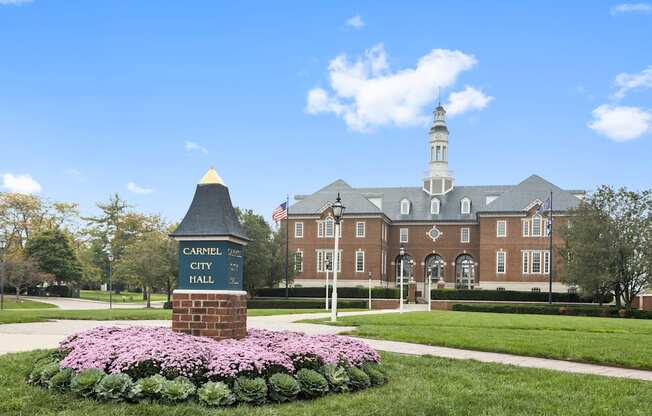 a brick building with a sign in front of a lawn with flowers