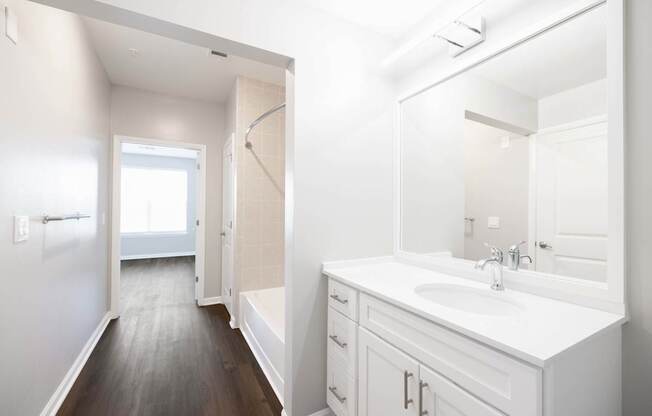 A white bathroom with a sink, mirror, and wooden floor.