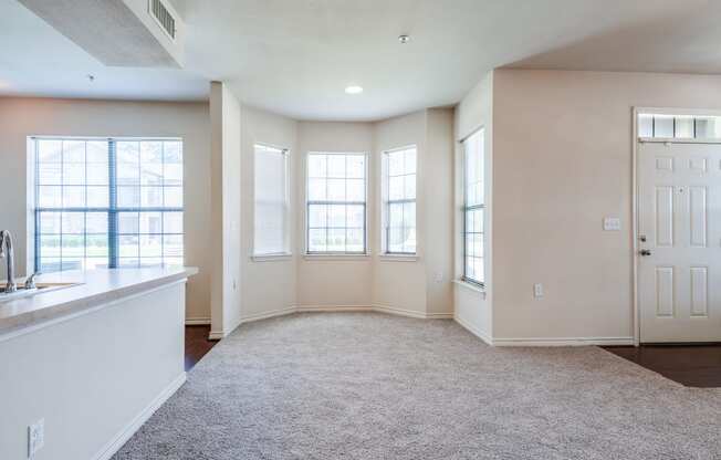 an empty living room with windows and a kitchen