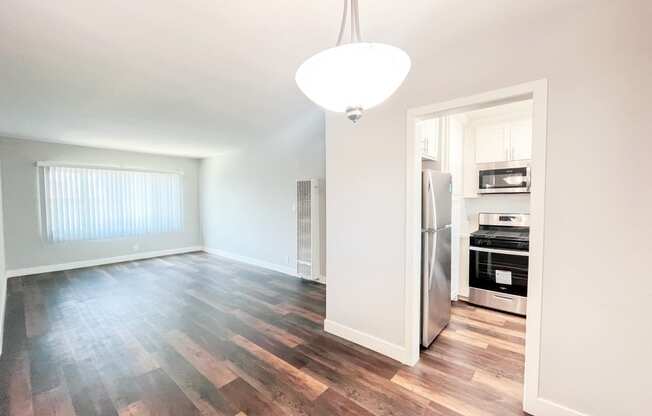 an empty living room and kitchen with wood flooring and a refrigerator