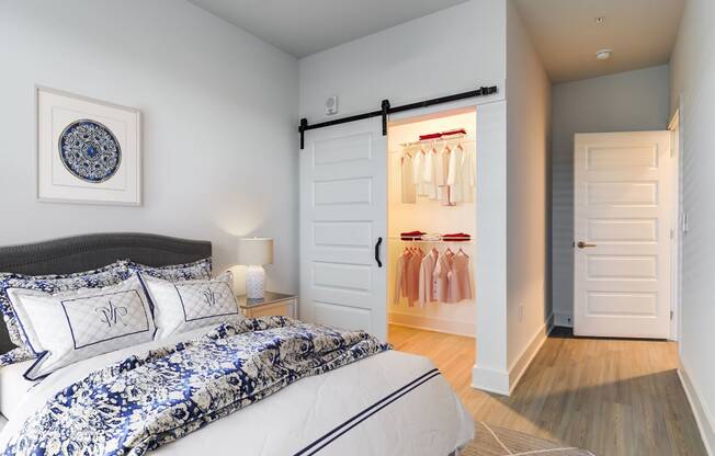 Pet-Friendly Apartments In Huntsville, AL - The Collins - Spacious Bedroom With Wood-Style Flooring, Area Rug, Bed, Nighstand with Lamp, High Ceilings, And A Large Closet With A Sliding Door