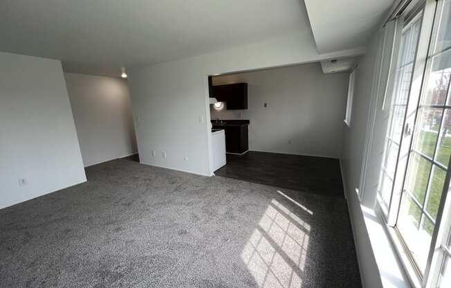 an empty room with a large window and a kitchen in the background