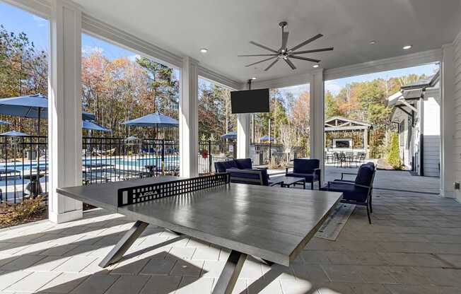 A table is in the middle of a patio with a pool and trees in the background.