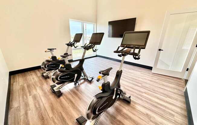 A room with a row of stationary bikes and a TV mounted on the wall.