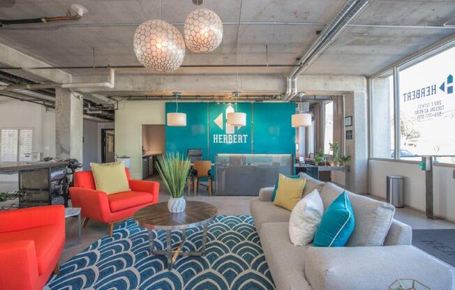 A living room with a blue and white patterned rug, a grey couch, a red chair, and a wooden coffee table.