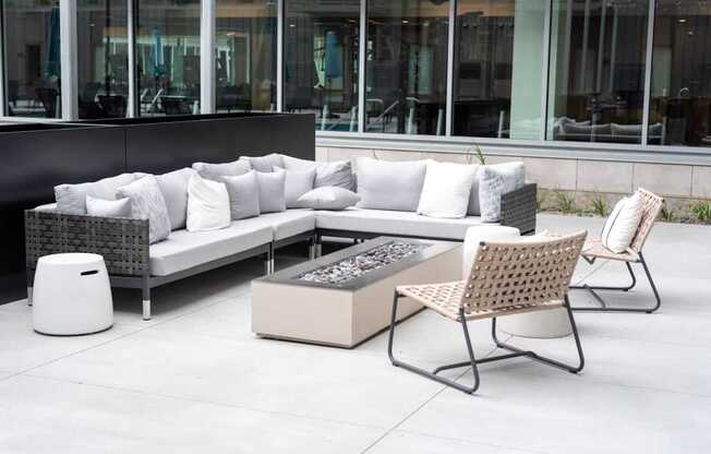 A patio furniture set with a white couch, pillows, and a fire pit.