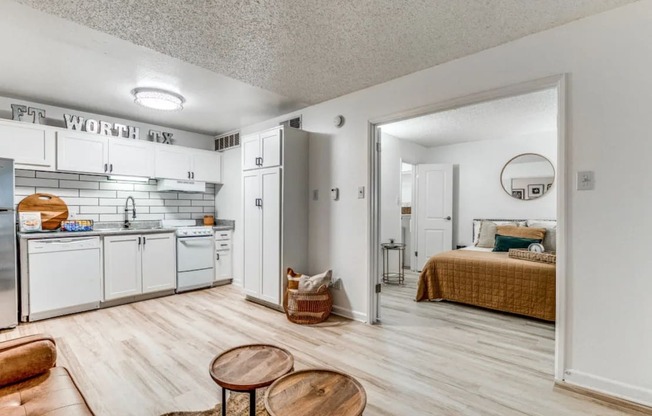 Fusion Fort Worth renovated kitchen area in Haltom City, TX with light wood plank flooring and subway tile backsplash, white appliances, and large bedroom door.