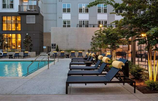 a row of lounge chairs next to a swimming pool in front of an apartment building