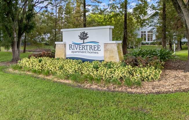 A sign for Rivertree Apartment Homes is surrounded by greenery.