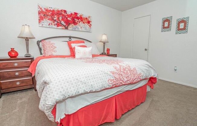 View of bed in model apartment bedroom with red painting on the wall at Laurel Parc apartments in Shreveport, LA.