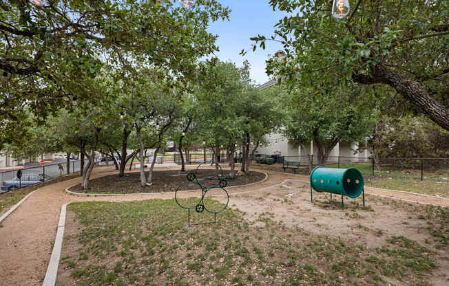 A playground with a swing set and a green barrel.
