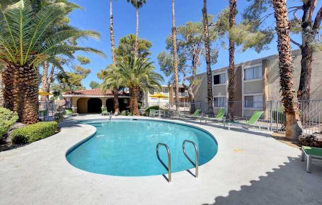 A pool surrounded by palm trees and a building in the background.