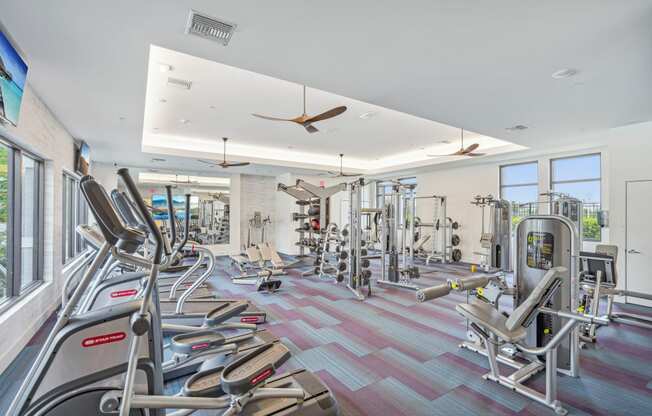 a gym with cardio machines and weights on the floor and windows