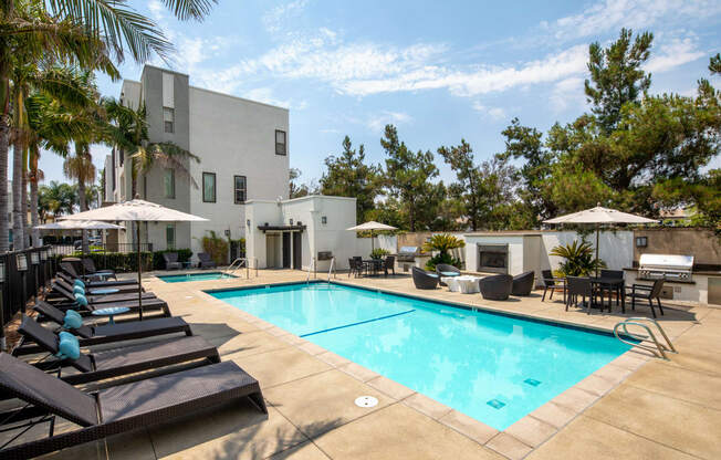 A pool area with lounge chairs and umbrellas in front of a white building.