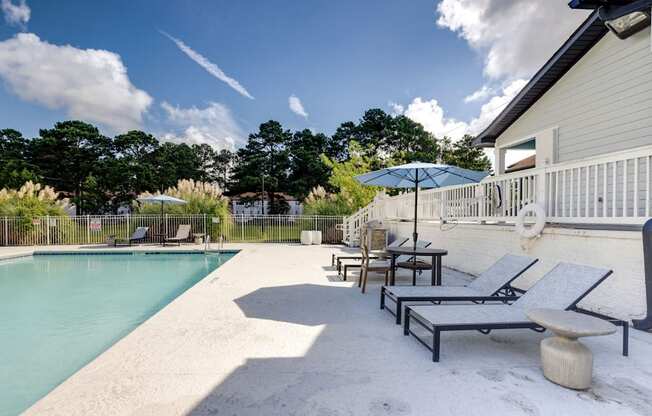 A pool area with sun loungers and a white building.