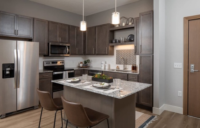 A modern kitchen with a stainless steel refrigerator, microwave, and dining table set for two.
