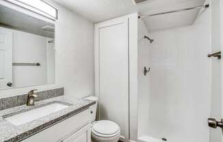 A white bathroom with a sink, toilet, and shower.