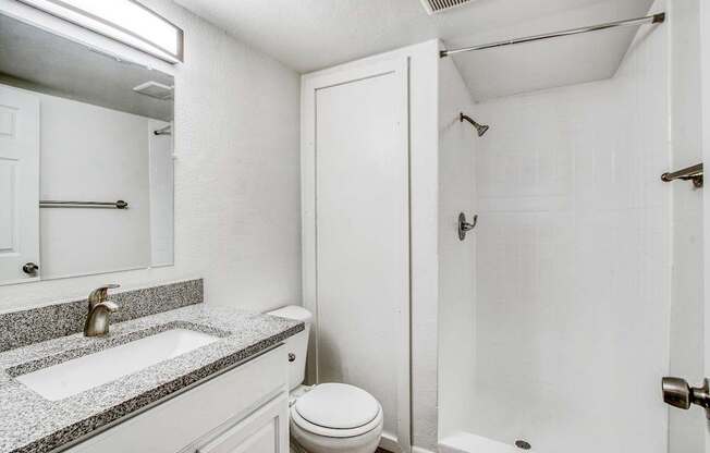 A white bathroom with a sink, toilet, and shower.