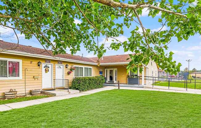 the front yard of a yellow house with a yard and a fence