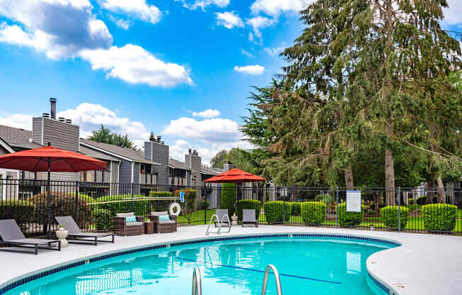 a swimming pool with umbrellas and chairs in front of apartment buildings