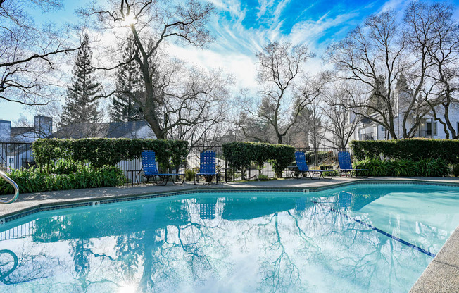 a swimming pool with blue chairs and trees in the background