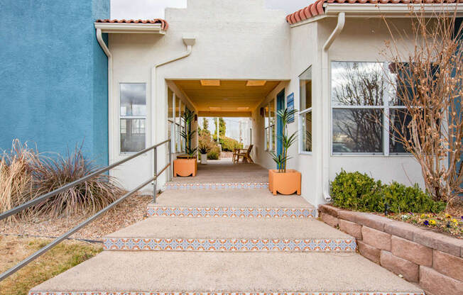 a building with a porch and stairs with potted plants on either side