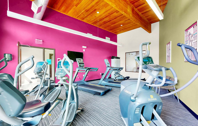 A gym with exercise equipment and a pink wall.