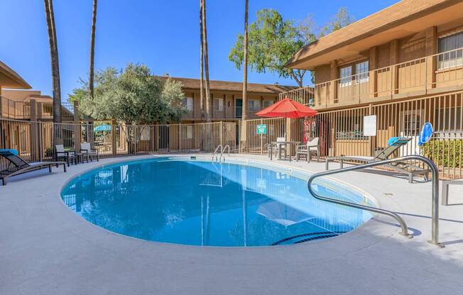 A swimming pool in a resort with a red umbrella.