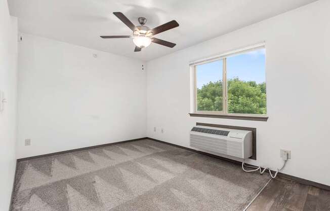 A room with a ceiling fan and a window with an air conditioner unit under it.
