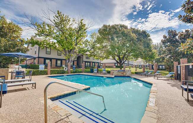 A swimming pool surrounded by a patio area with chairs and trees.
