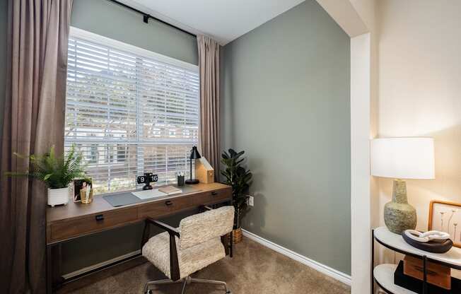 A room with a desk, chair, and a window with blinds.