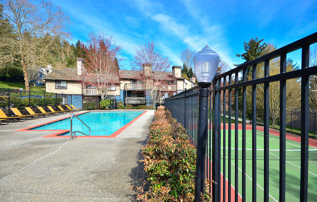 A pool and tennis court are surrounded by a black fence.