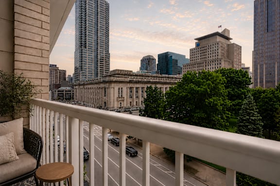 A balcony with a chair and table overlooking a city street.