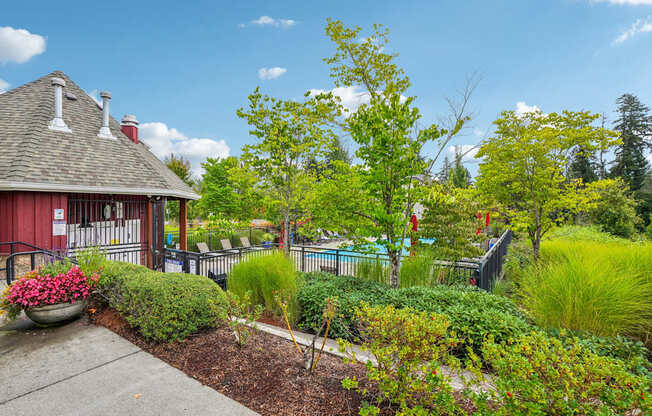A red building with a grey roof and white chimneys is surrounded by a garden with a variety of plants and trees.