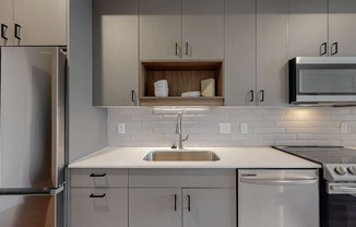 A modern kitchen with a stainless steel refrigerator, a white sink, and a microwave above the stove.