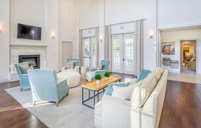 Interior of the clubhouse with ample seating, an ottoman, tables, high windows, high ceiling, and access to outside at Evergreens at Mahan apartments  in Tallahassee, FL
