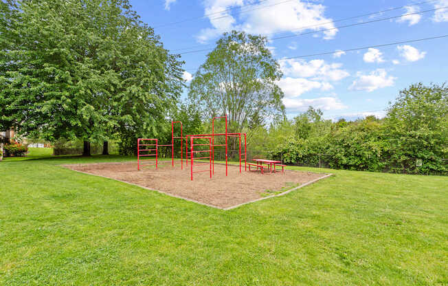 A playground with a red swing set in the middle of a grassy area.