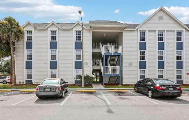 Two cars are parked in a parking lot in front of a white building with blue trim.