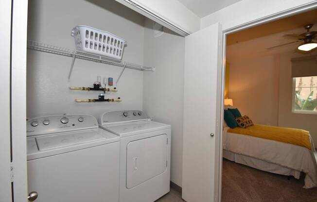 A small laundry room with a washer and dryer and a bedroom with a bed and a window.