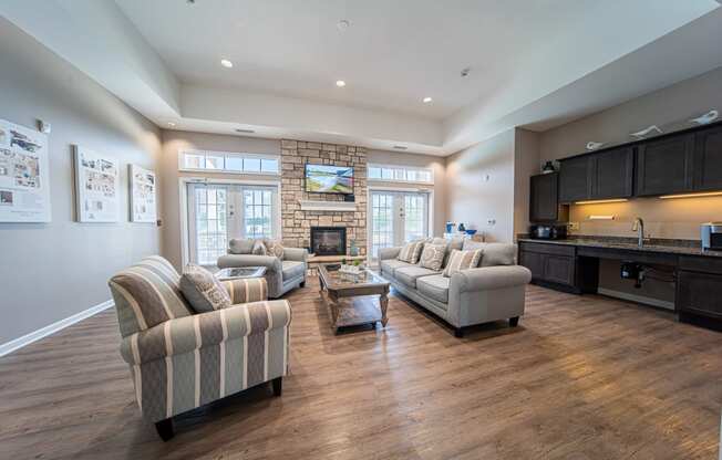 Inside clubhouse, high ceilings, striped grey furniture, fireplace and TV along back wall, windows on the left and right side of frireplace.