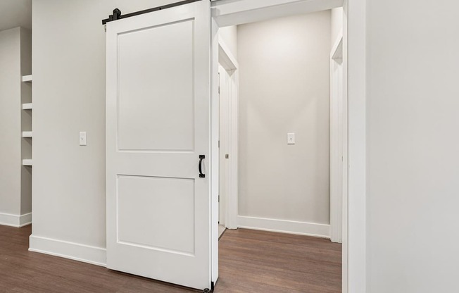 A white door with a black handle is open. that leads to bedroom and bathroom
