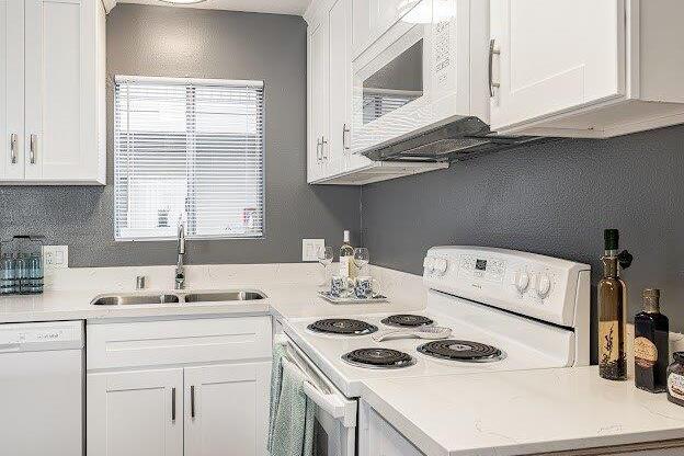 A white kitchen with a stove, sink, and cabinets.
