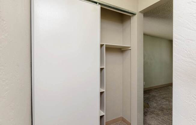 A white closet with a shelf and a door open.