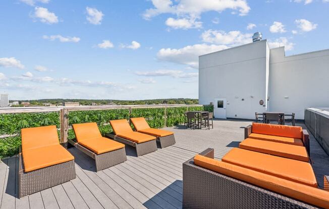 a rooftop deck with orange lounge chairs and a building in the background