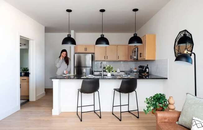 A woman is standing in a kitchen with a white countertop and black barstools.